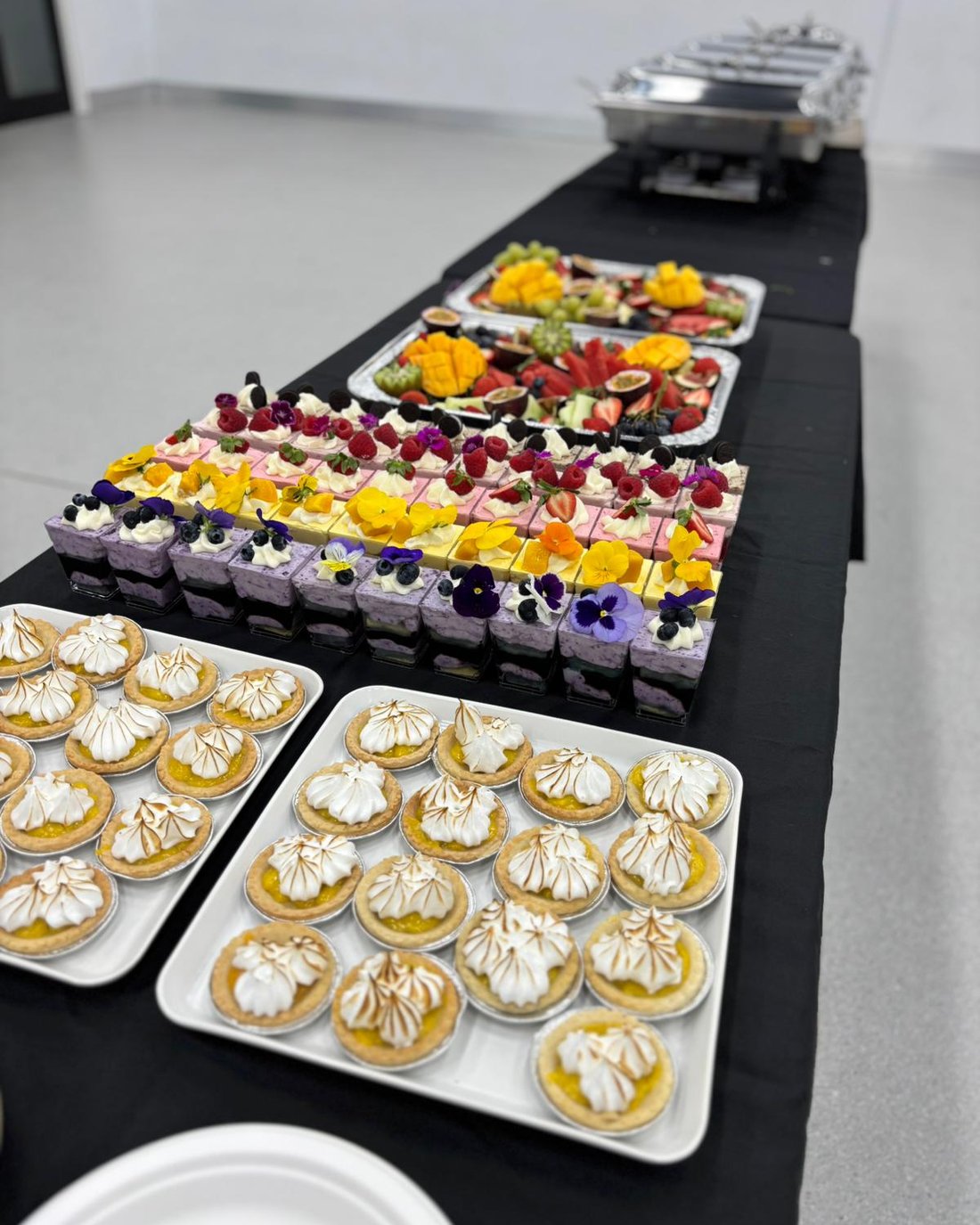 Catered event spread with dessert cups, lemon meringue tarts and fruit platters